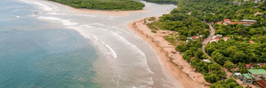 Aerial view of Tamarindo Beach with a curved shoreline, calm waters, and lush tropical landscape in Culebrabordered by dense green vegetation and small buildings along the coast.