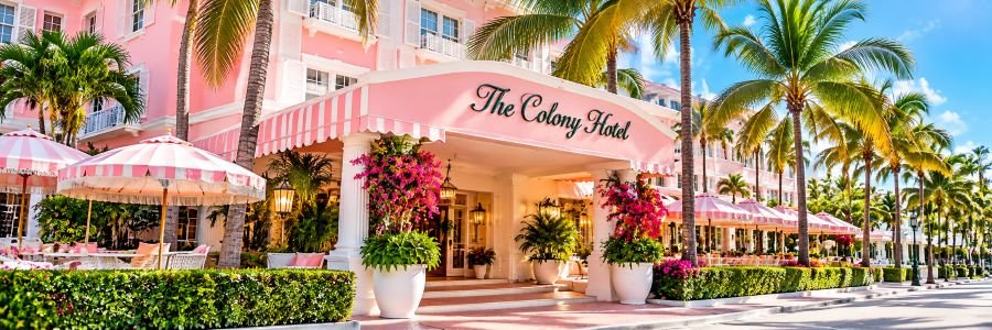 The Colony Hotel in Palm Beach, Florida, featuring its iconic pink exterior, palm trees, tropical landscaping, and outdoor seating