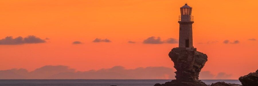 Tourlitis Lighthouse silhouetted against a colorful sunset sky on Andros Island, Greece.