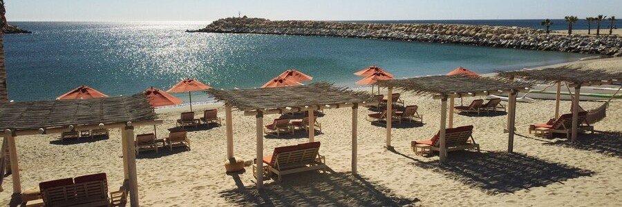 Beach loungers and shaded cabanas at Veleros Beach Club in Los Cabos overlooking calm ocean water and sunny coastal views.
