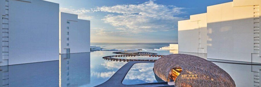 Modern infinity pool at Viceroy Los Cabos with white architecture, reflecting water, and ocean views at sunset.
