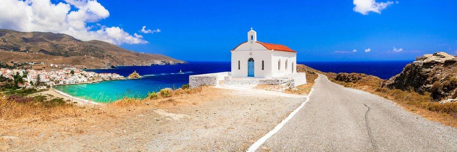 White chapel overlooking a turquoise bay and coastline on Andros Island, Greece.