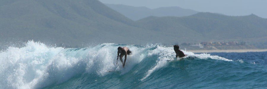 Cabo Beaches at Zippers Beach with surfers riding blue waves beneath the mountains near San José del Cabo