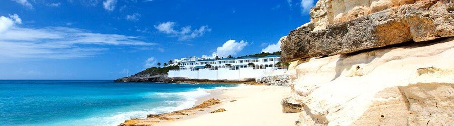 Rocky coastal cliffs and a white beachfront resort overlooking turquoise Caribbean water.