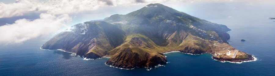 Aerial view of Saba Island with dramatic volcanic slopes, rugged coastline, and surrounding deep blue Caribbean Sea.