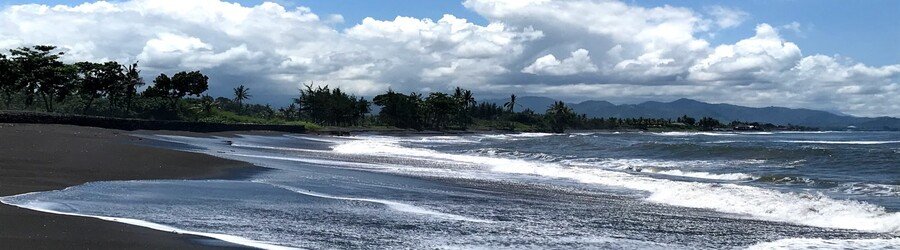 Black sand shoreline on Saba with waves rolling in beneath cloudy skies and mountain views