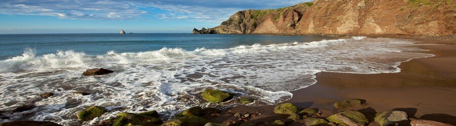 Rocky coastal beach on Saba with waves washing over stones at the base of steep cliffs