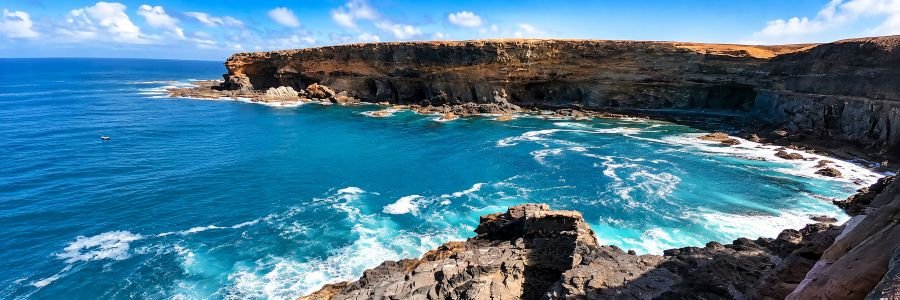 Dramatic volcanic cliffs and turquoise Atlantic waves along the Ajuy Caves coastline in Fuerteventura, Canary Islands.