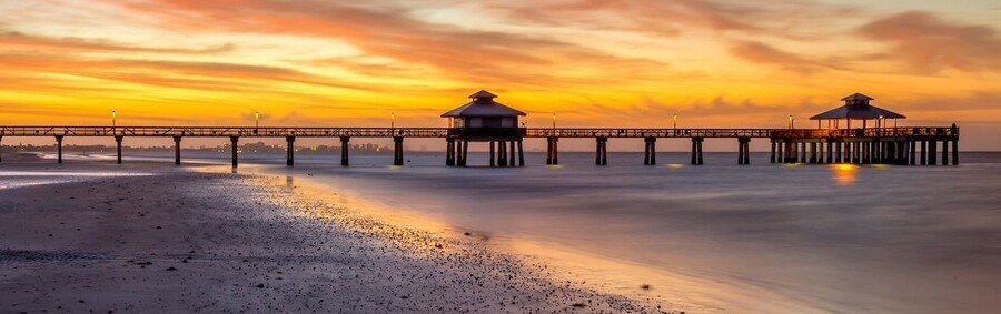 Fort Myers Beach pier at sunset with calm Gulf waters and golden sky