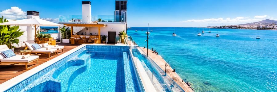 Rooftop swimming pool with blue mosaic tiles, comfortable sun loungers, glass railings, and beautiful turquoise ocean views.