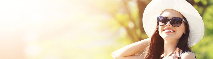 Woman wearing dark sunglasses and a wide-brim sun hat smiling in bright outdoor sunlight.