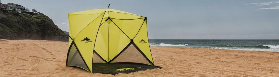 Bright yellow beach umbrella tent providing shade on sandy shore with ocean waves in the background.