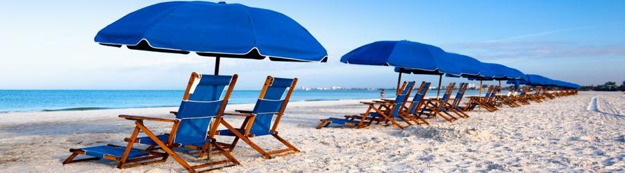 Blue beach umbrellas with lounge chairs lined up on the sand, perfect for shade and relaxation by the ocean.