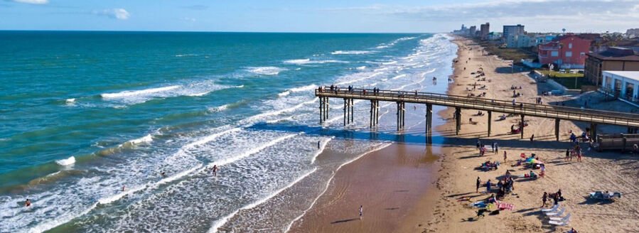 Aerial view of South Padre Island beach with pier, Gulf waves, and beachfront buildings along the Texas coast