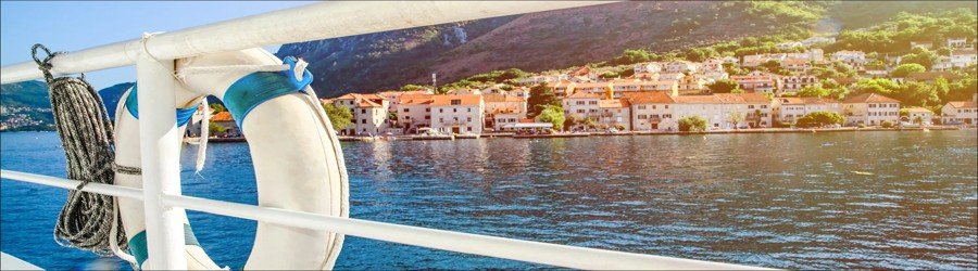 Lifebuoy and boat railing overlooking a charming coastal town with red-roofed buildings and calm ocean water — perfect scene for planning and booking a cruise.