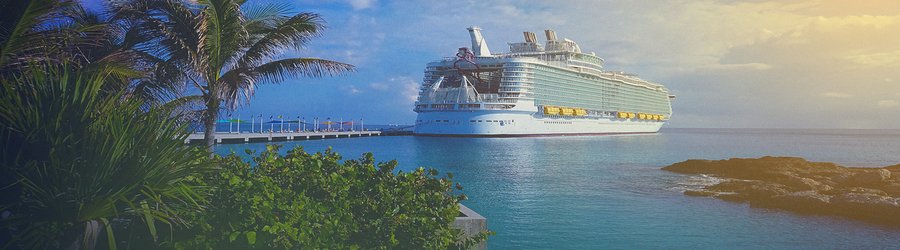 Luxury cruise ship docked near lush palm trees and rocky shoreline under a vibrant tropical sky.