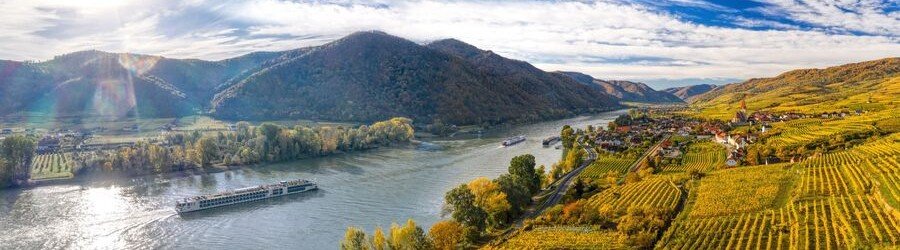 River cruise ship sailing through the Wachau Valley near Dürnstein, Austria, surrounded by vineyards and rolling hills.