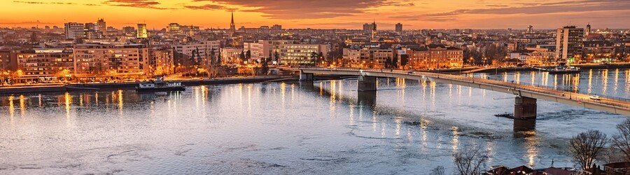 Evening view of Novi Sad, Serbia, with illuminated bridges and city lights reflecting on the Danube River.