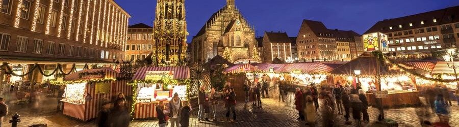 Visitors exploring the festive Nuremberg Christmas Market with illuminated stalls and historic buildings in Germany.