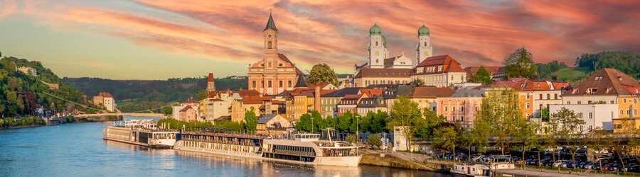 River cruise ships docked along the Danube River in Passau, Germany, beneath the city's historic skyline.