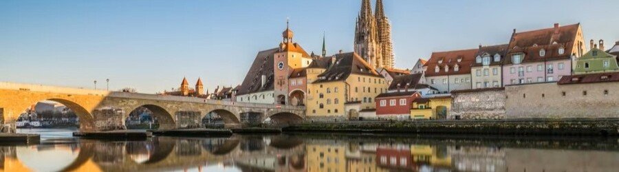 Historic stone bridge and medieval waterfront buildings along the Danube River in Regensburg, Germany.