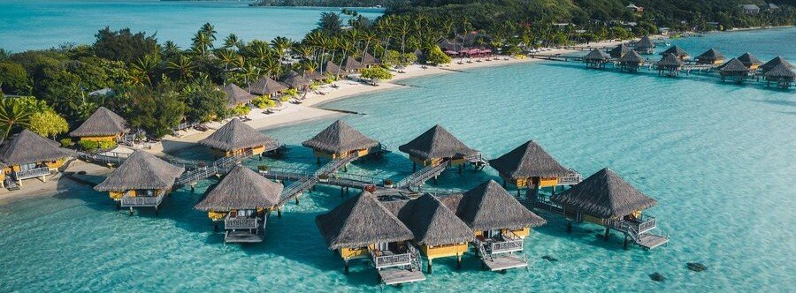 Aerial view of overwater bungalows in Bora Bora with clear turquoise lagoon and tropical shoreline