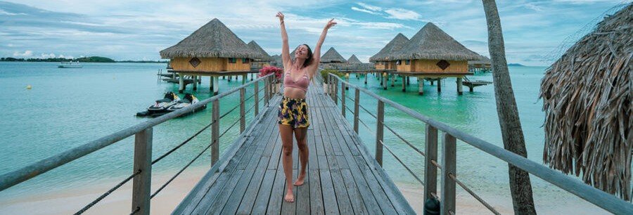 Woman standing on wooden boardwalk near overwater bungalows in Bora Bora lagoon with turquoise water