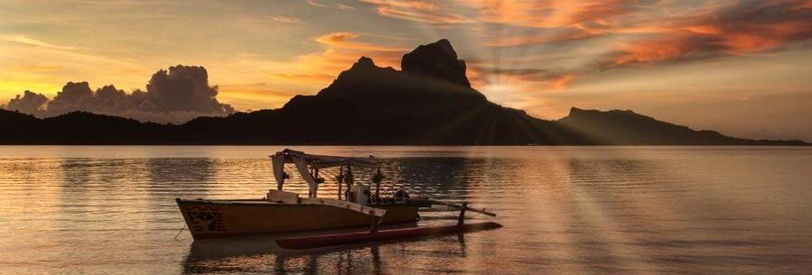 Traditional Polynesian canoe at sunset in Bora Bora lagoon with Mount Otemanu silhouette and colorful sky