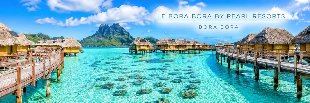 Overwater bungalows at Le Bora Bora by Pearl Resorts overlooking a crystal-clear turquoise lagoon, wooden walkways, and Mount Otemanu in the distance.