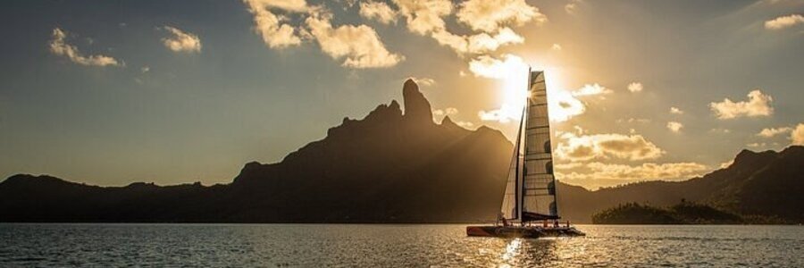 Catamaran sailing at sunset near Matira Beach in Bora Bora with golden sky and mountain silhouette