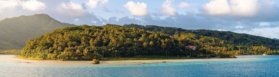 Motu islet in Moorea surrounded by turquoise lagoon water with lush tropical vegetation and mountains in the background