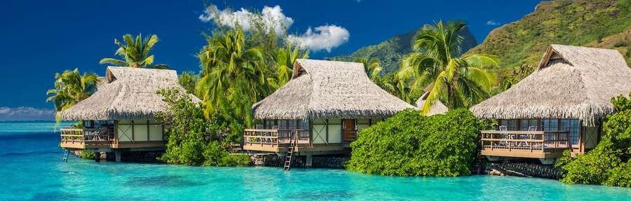 Overwater bungalows in Moorea with turquoise lagoon water and lush green mountains in the background