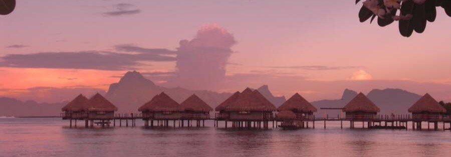 Overwater bungalows in Moorea at sunset with pink sky and calm lagoon