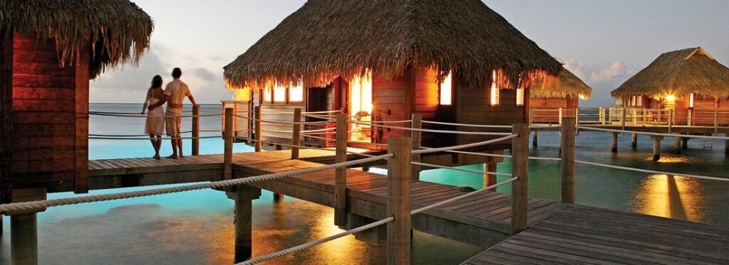 Couple walking near overwater bungalows in Moorea at sunset with lagoon views