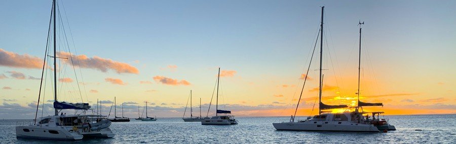Sailboats anchored in Tahiti lagoon at sunset with golden sky