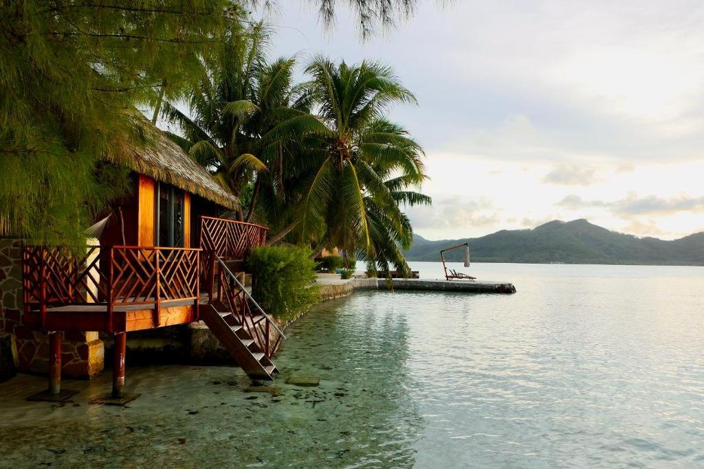 Overwater bungalow with palm trees and lagoon view at Eden Private Island Tahaa