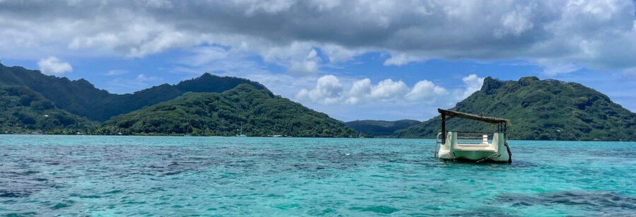 Outrigger boat floating in turquoise lagoon with lush mountains in Huahine, French Polynesia