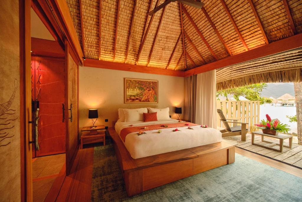 Overwater bungalow bedroom with terrace view and lagoon at Le Taha’a by Pearl Resorts