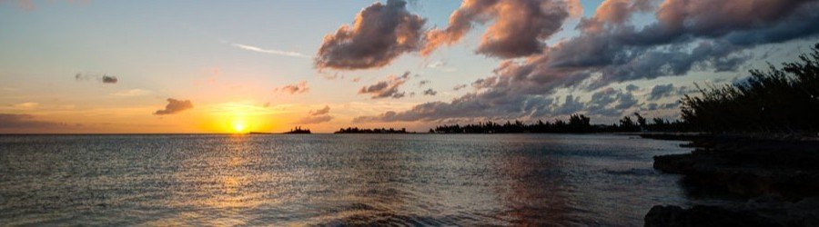 Colorful sunset over calm ocean waters with silhouetted shoreline and clouds.