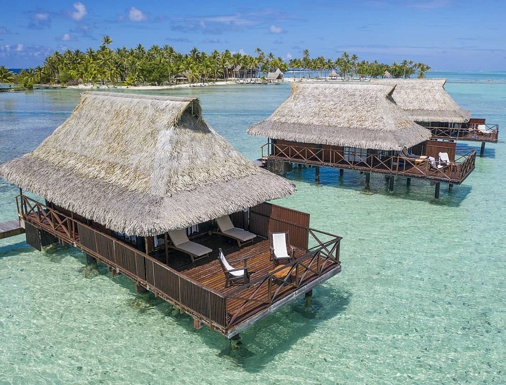 Overwater bungalows with thatched roofs in shallow lagoon at Vahine Private Island