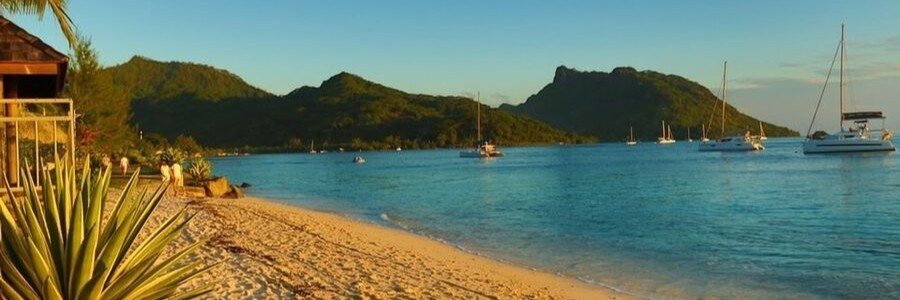 Beach house overlooking lagoon with sailboats and mountains at sunset in Huahine, French Polynesia