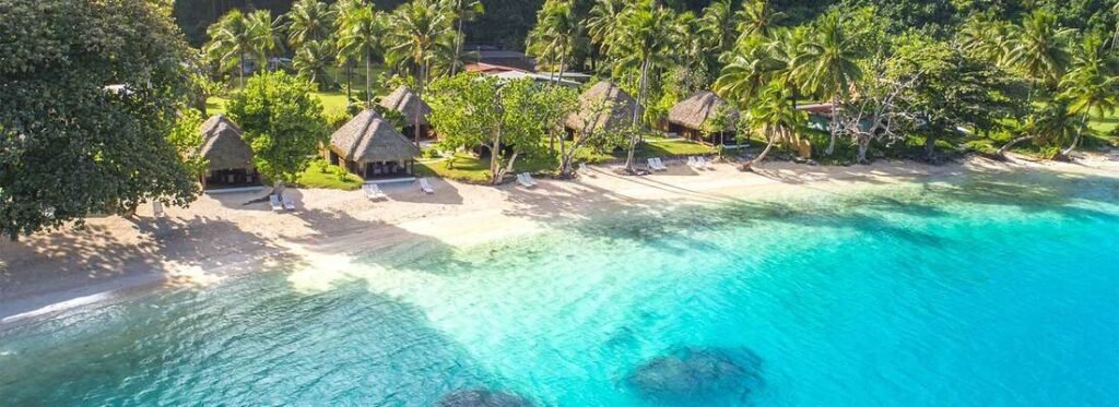 Aerial view of beachfront bungalows and palm trees along a turquoise lagoon in Huahine, French Polynesia