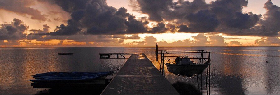 Sunset over a calm lagoon in Raiatea with a wooden dock and boats under a golden sky