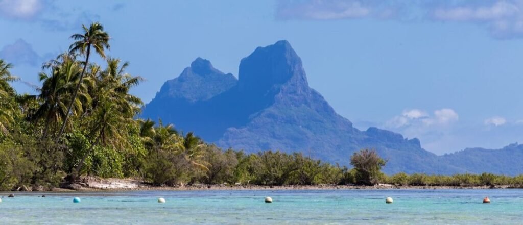 Turquoise lagoon with palm trees and dramatic mountain peaks in Taha’a French Polynesia