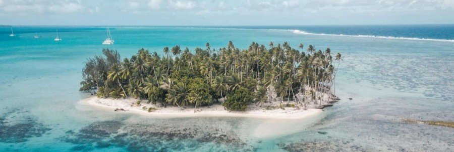 Aerial view of a tropical motu in Taha’a lagoon with white sand beach, palm trees, and turquoise water