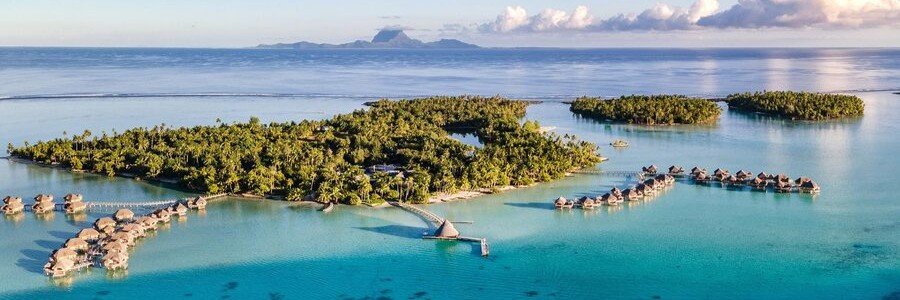 Overwater bungalows on a tropical motu surrounded by clear lagoon in Taha’a, French Polynesia