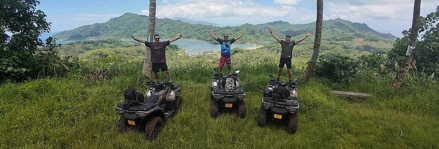 Travelers on quad bikes at a mountain viewpoint overlooking lush valleys and lagoon in Tahaa