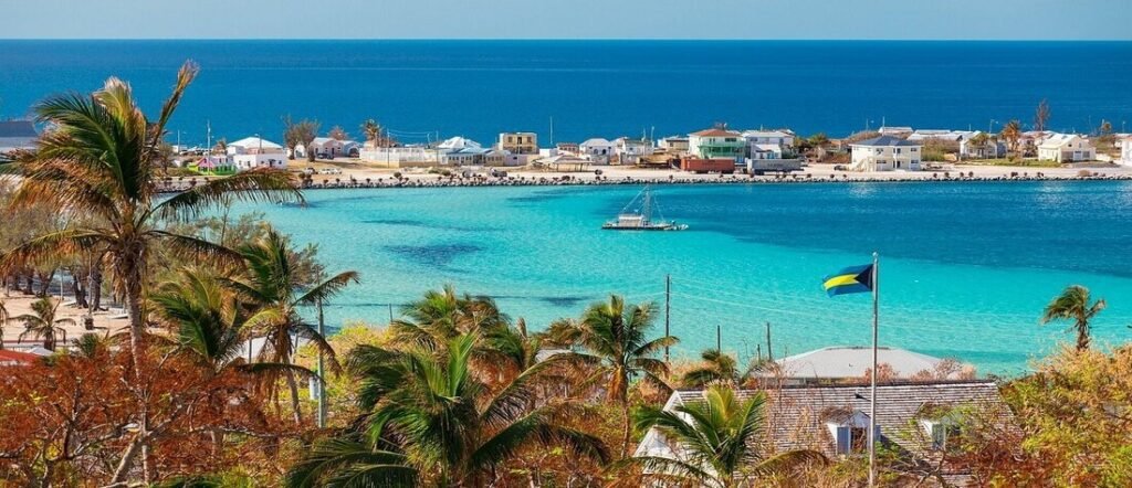 Colorful island settlement overlooking a bright turquoise harbor with boats and palm trees.