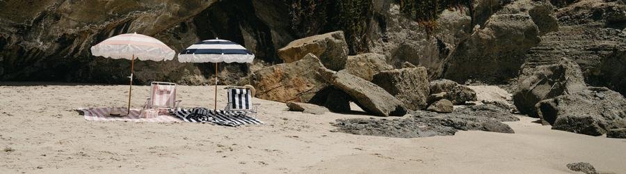 Tommy Bahama striped beach chairs with matching umbrellas on a sandy beach by the rocks.