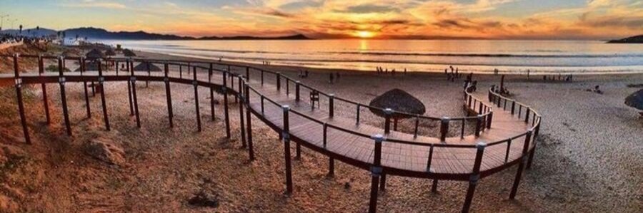 Ensenada beaches at sunset with a wooden boardwalk leading across sandy shores, glowing golden sky, silhouettes of visitors, and calm Pacific Ocean views at Playa Hermosa in Baja California Mexico